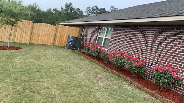 A yard with red mulch around a flower bed and small tree