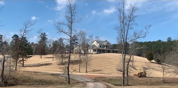 A large house sitting on a hill with acres of grass freshly mowed surrounding it.